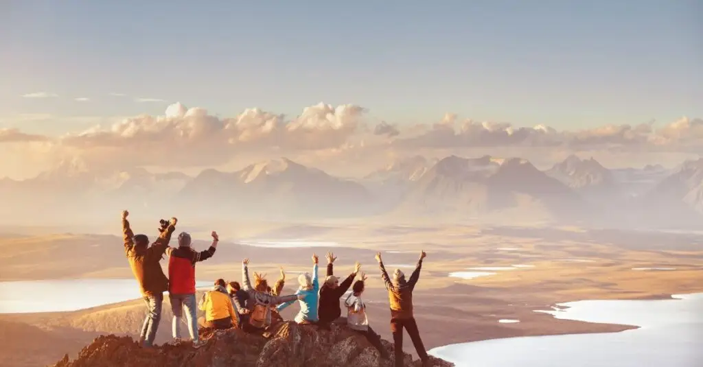 A group of people standing on a mountain summit overlooking a vast landscape, celebrating together and representing the power of diverse strengths working toward a shared goal.